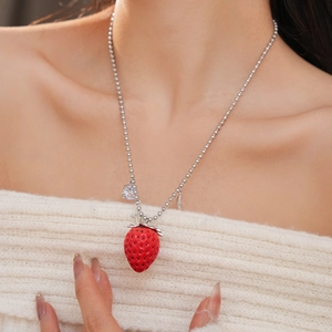 Dettaglio della collana con pendente a fragola rossa e zircone su modella con maglione bianco