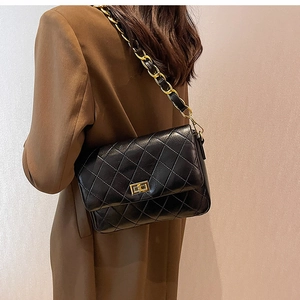 Detail of black quilted leather shoulder bag with gold chain strap and metal clasp
