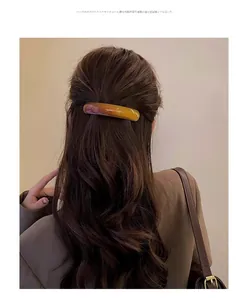 Model wearing a large amber tortoiseshell hair clip on dark brown wavy hair back view