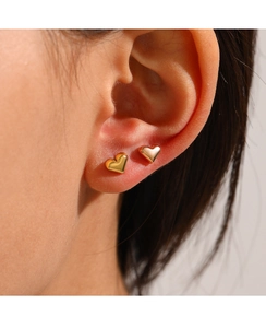 Gros plan de boucles d'oreilles cœur dorées polies sur un modèle au look minimaliste