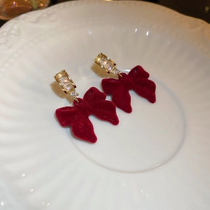 Dettaglio di orecchini a fiocco in velluto rosso vino con cristalli su piatto bianco