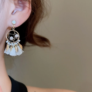 Detail shot of dreamcatcher style earrings with white tassels and gold leaf charms