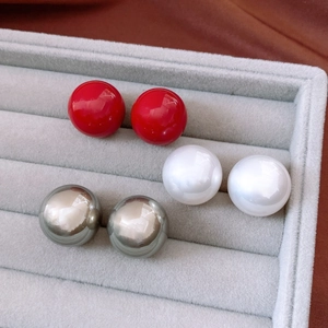 Detailed view of spherical pearl earrings in red, white and silver on a velvet tray