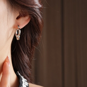 Close-up of silver hollow four-leaf clover earrings showing intricate link design and metal luster