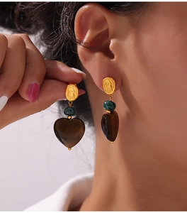 Detail of heart-shaped earrings with tiger eye stone pendant on model showing craftsmanship