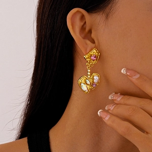 Detail of vintage gold earrings with pink gemstones, pearls, and diamonds on a model