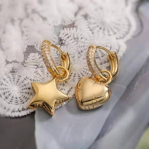 Macro detail of asymmetric gold heart and star earrings with pavé cubic zirconia