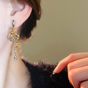 Detail of silver snake-shaped earring with yellow accents and a clear teardrop zircon on model