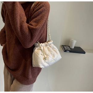 Detail of cream quilted chain bag with gold metal ball pendant on a textured surface