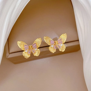 Detailed close-up of golden butterfly earrings with pink and clear zircons on a jewelry box