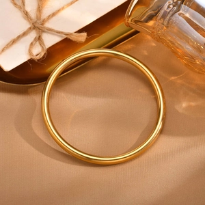 Minimalist gold stainless steel bangle bracelet on elegant beige silk background