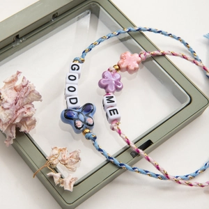 Detailed view of handmade woven bracelets with ceramic flower and letter charms on a display stand