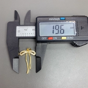 Macro shot showing digital caliper measuring a 19.6mm gold zircon bow pendant