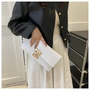 Close-up of white crocodile embossed clutch bag featuring a gold H-shaped metal buckle