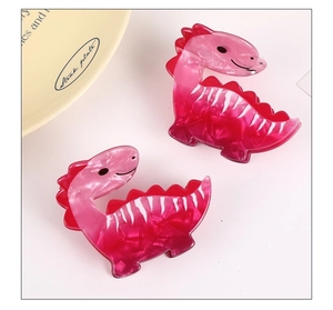 Detail view of two cute pink gradient dinosaur acetate hair claws on a cream background