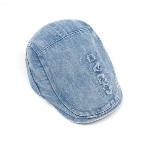 Detail of light blue washed denim flat cap with large white vintage embroidered letters