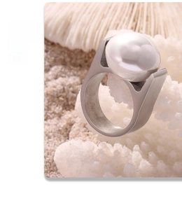 Macro shot of wide titanium ring with a large baroque pearl on white coral and sand