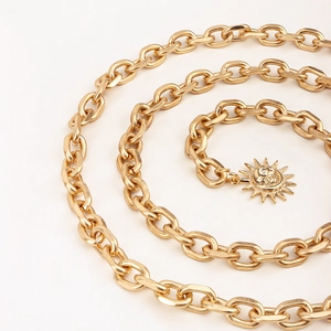 Close-up of golden metal chain belt with sun smiley pendant on white background