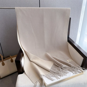 Detailed texture of beige cashmere-feel scarf with fringe hanging on a wooden chair