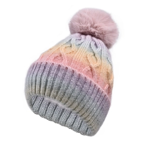 Detail of cable knit pattern and pink faux fur pompom on a gradient winter beanie hat