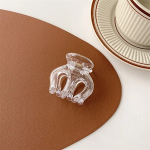 Detailaufnahme einer transparenten Haarklammer auf braunem Leder mit Kaffeetasse