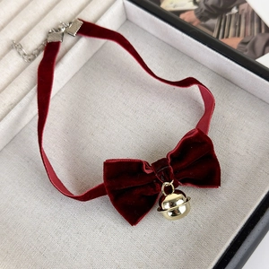 Détail du choker en velours bordeaux avec nœud et clochette dorée sur plateau en lin