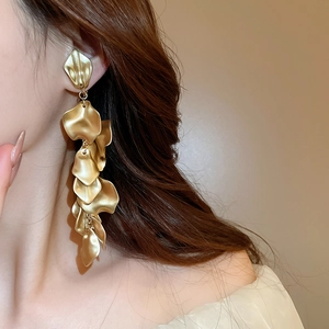 Detail shot of elegant long golden matte metal flower petal tassel earrings on model