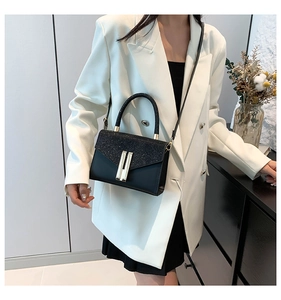 Detail of square black crossbody bag with glitter flap and gold buckle on white suit