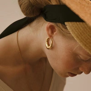 Close-up of minimalist 18K gold plated thick hoop earrings worn by a model in soft light