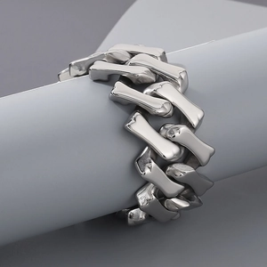 Close-up of a bold silver stainless steel Cuban chain bracelet on a minimalist gray stand