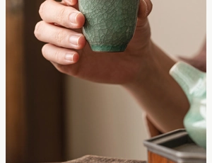 Close-up of hand holding a celadon ceramic tea cup with a distinct ice crackle glaze finish