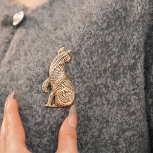 Detailaufnahme einer Vintage-Metall-Katzenbrosche auf einem grauen Strickpullover