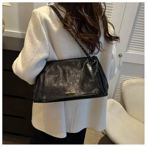 Detail of black glossy chain bag showing texture and golden logo on shoulder