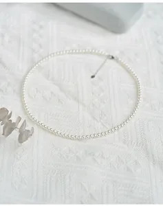 Detailed macro of 3mm white round pearl necklace with silver extension chain on white fabric