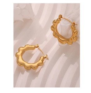 Macro shot of gold-plated hoop earrings with unique wavy texture on white background