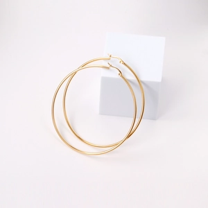Detail view of large gold minimalist hoop earrings resting on a white geometric prop