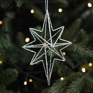 Silver star Christmas ornament with glitter finish hanging on a festive tree branch