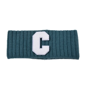 Détail du bandeau tricoté bleu sarcelle foncé avec un écusson lettre C blanc texturé