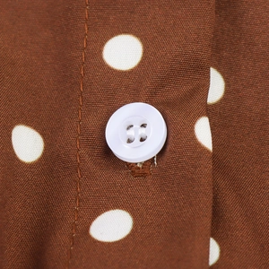 Nahaufnahme von braunem Polka-Dot-Stoff mit weißem Knopf und detaillierten Nähten