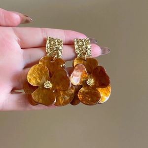 Close-up of amber resin flower earrings with gold metal accents worn on ear