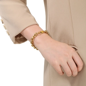 Gros plan d'un bracelet doré à maillons porté par un mannequin en costume beige