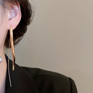 Macro detail of elegant gold-tone wavy drop earrings worn with a black suit jacket
