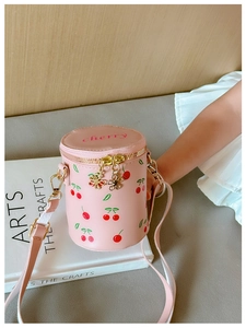 Detailed shot of pink cylindrical kids bag with cherry patterns and golden hardware