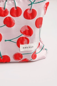 Close-up of red cherry print on pink canvas cosmetic bag with stitched brand label