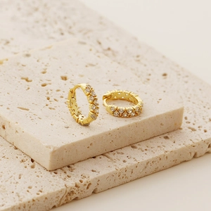 Detail of gold huggie hoop earrings with double-row cubic zirconia on stone display