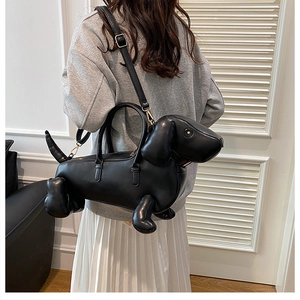 Detail of dachshund-shaped black crossbody bag with gold hardware shown on model