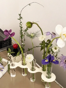 Detail of five glass test tube vases on white wavy base with fresh garden flowers