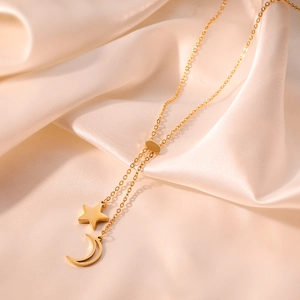 Golden star and moon pendant lariat necklace displayed on elegant beige silk fabric