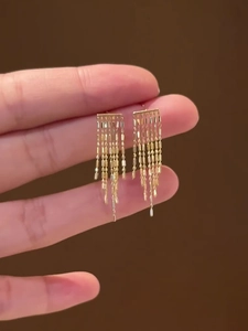 Gros plan sur des boucles d'oreilles dorées à franges avec de longues chaînes métalliques