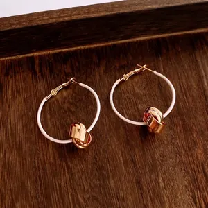 18K gold plated hoop earrings with white coating and gold knot charms on wood background